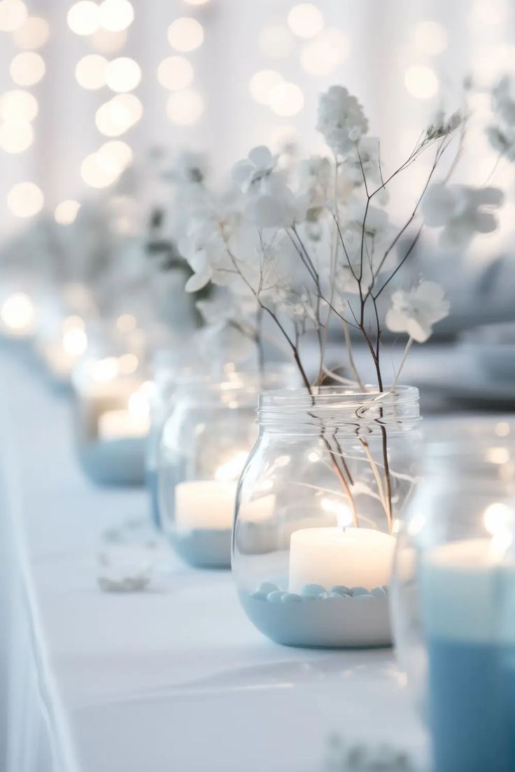 candles and flowers are in glass jars on a white tablecloth with lights behind them