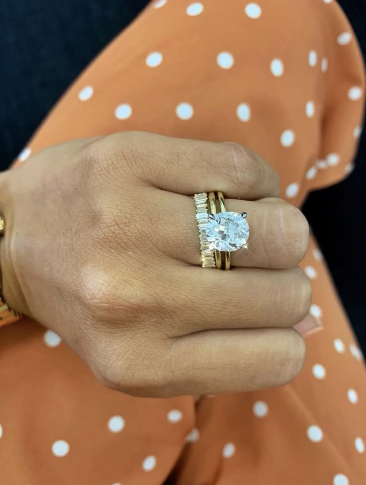 a woman's hand wearing a gold ring with a diamond in the center and white dots on it