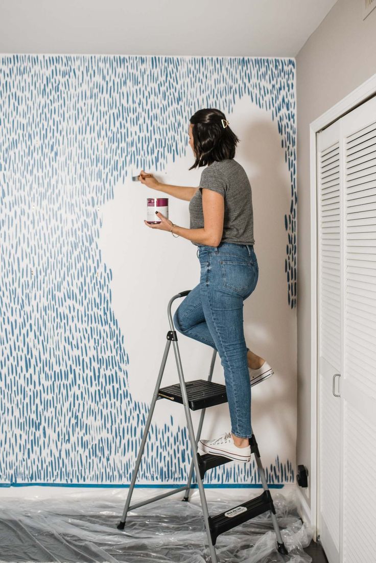 a woman is painting a wall with blue and white designs on it, while holding a paint roller