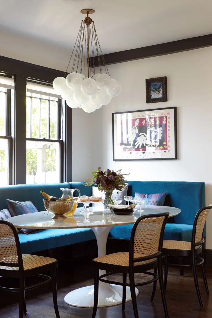 a dining room table with four chairs and a blue couch in front of two windows