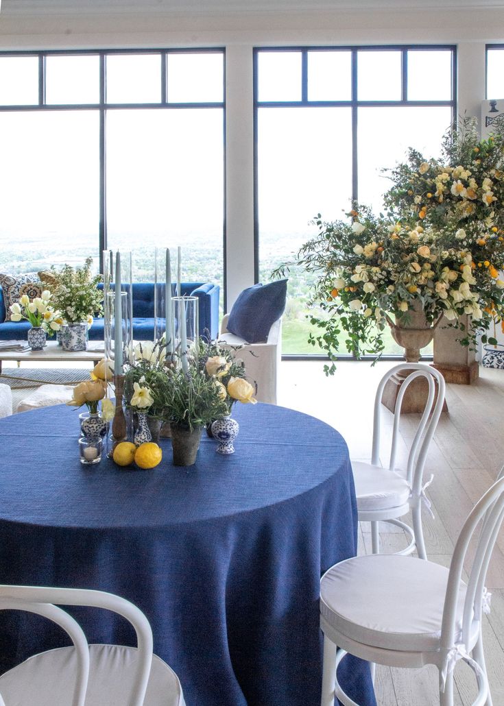 a blue table cloth with white chairs and yellow flowers in vases on the table