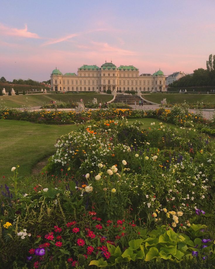 a large building with lots of flowers in the foreground and green grass around it