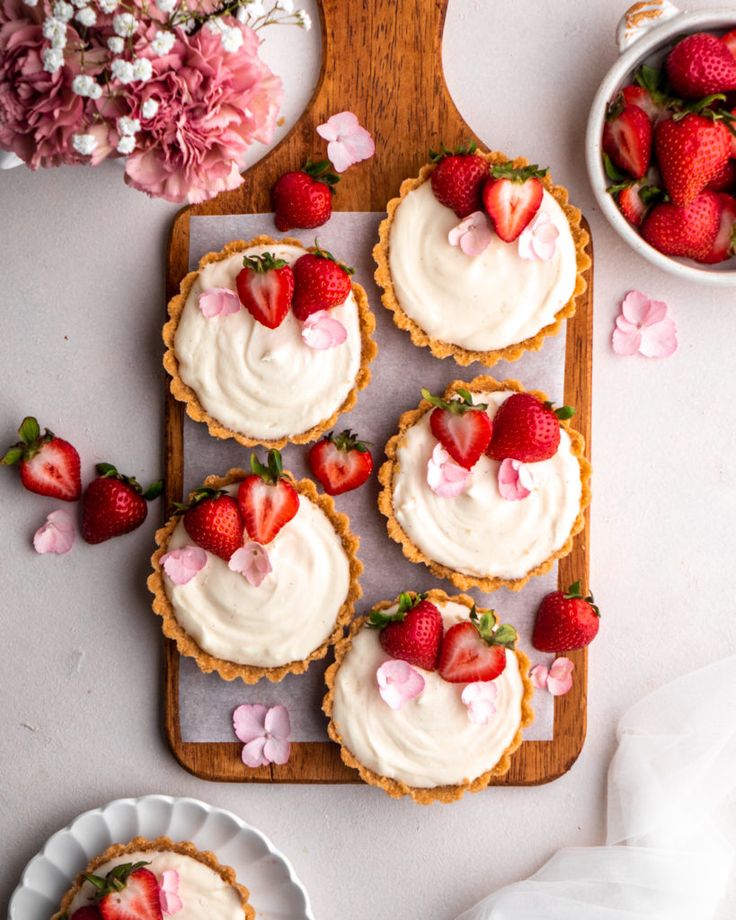 strawberry cupcakes with white frosting and fresh strawberries on the plate next to them