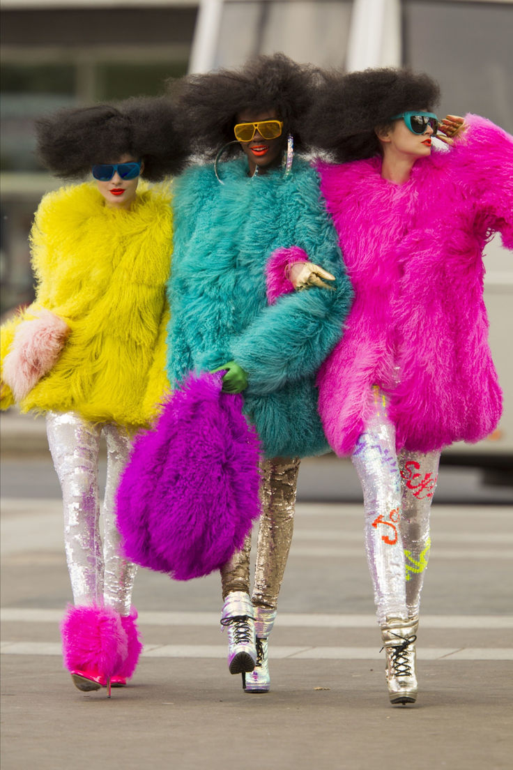 three women in brightly colored furs walking down the street