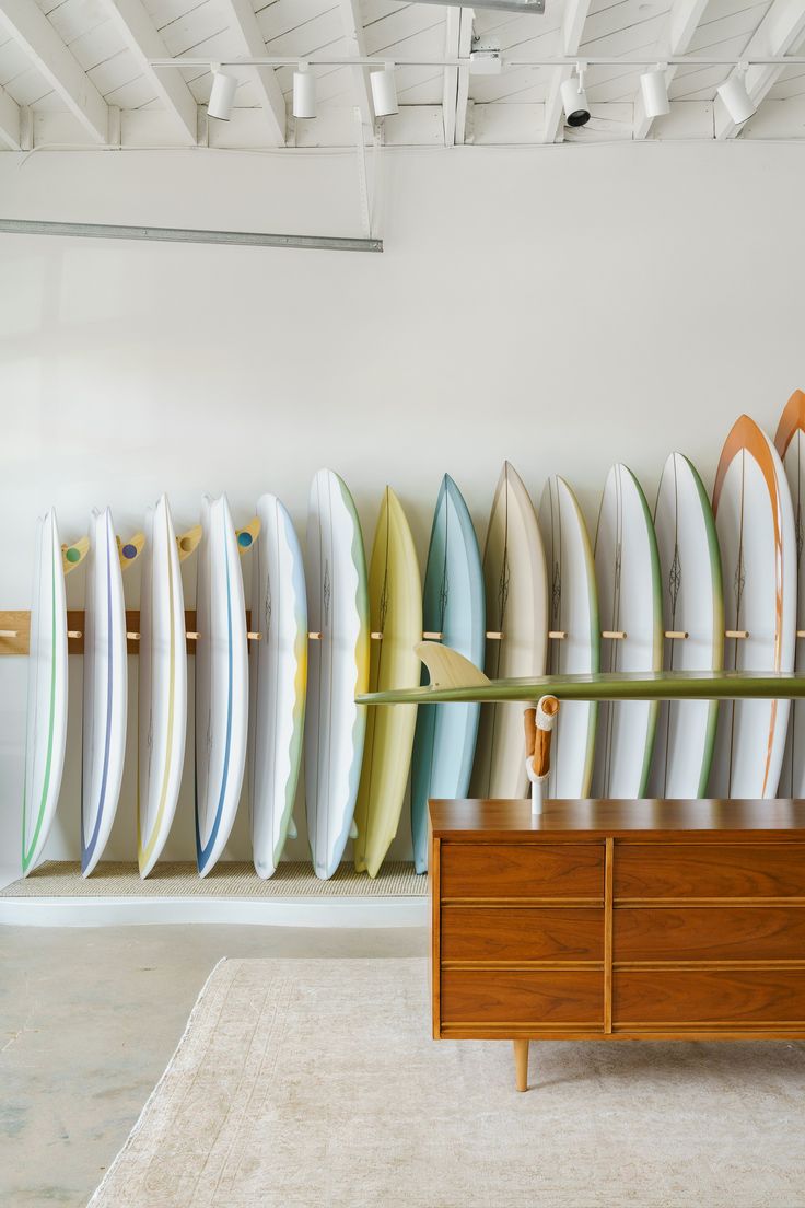 surfboards are lined up against the wall in a room with a dresser and rug