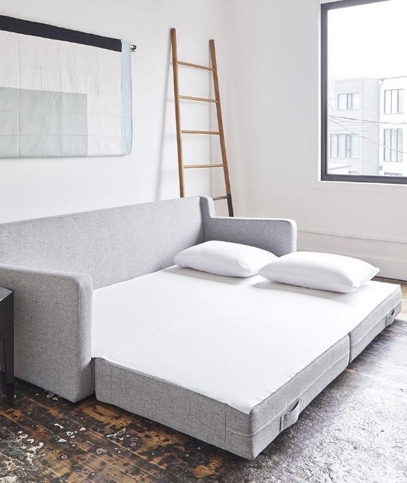 a couch with pillows on it in front of a window and a ladder leaning against the wall