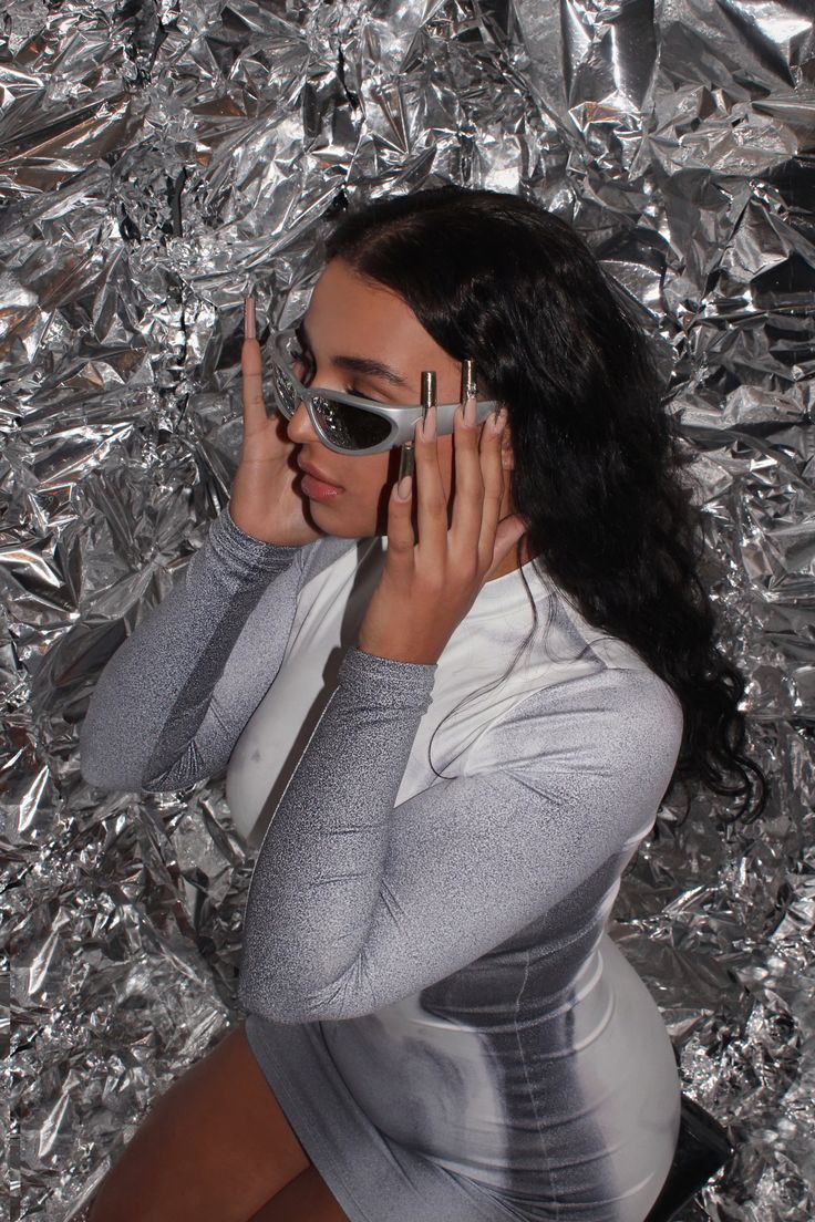 a woman wearing sunglasses and holding her hands up to her face while sitting on tin foil