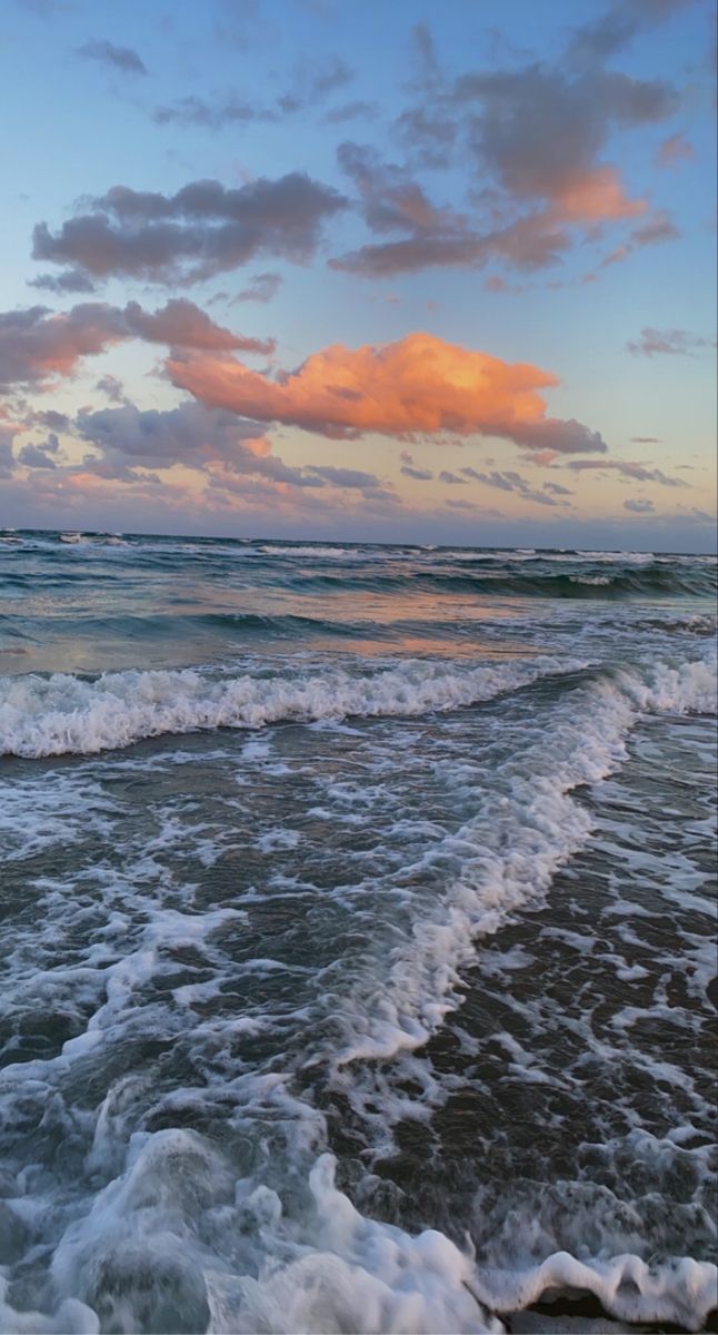 the ocean waves are rolling in to shore at sunset time with pink and blue clouds