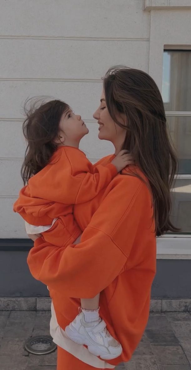 a woman in an orange hoodie holding a small child on her back and looking at each other