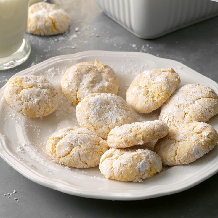 a plate full of powdered sugar cookies next to a glass of milk on a table