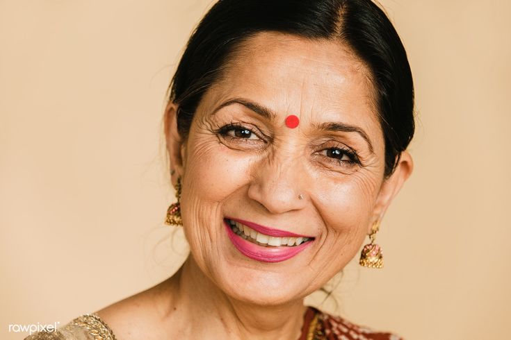 an older woman smiling for the camera with her eyes wide open and wearing gold jewelry