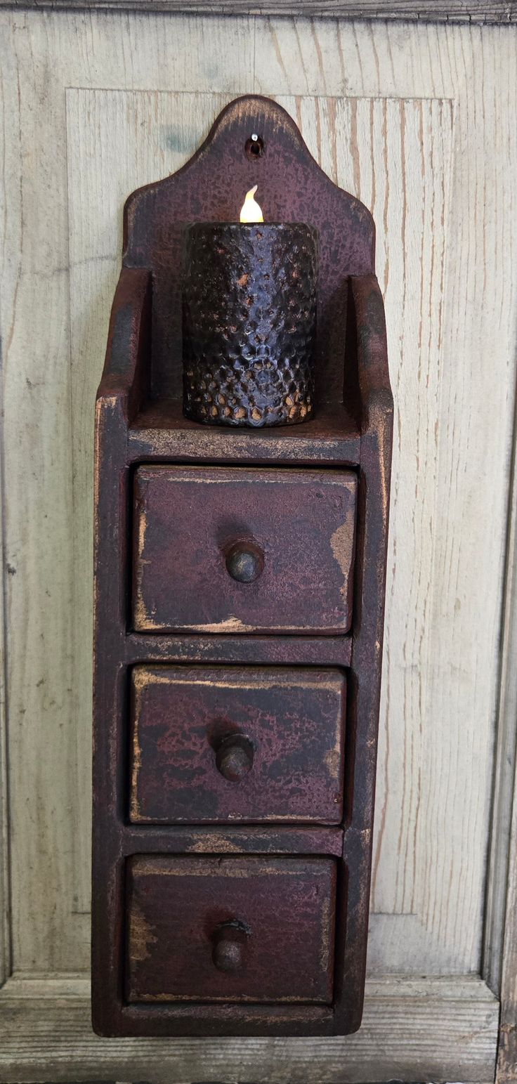 an old wooden cabinet with two drawers and a candle holder on the front door handle