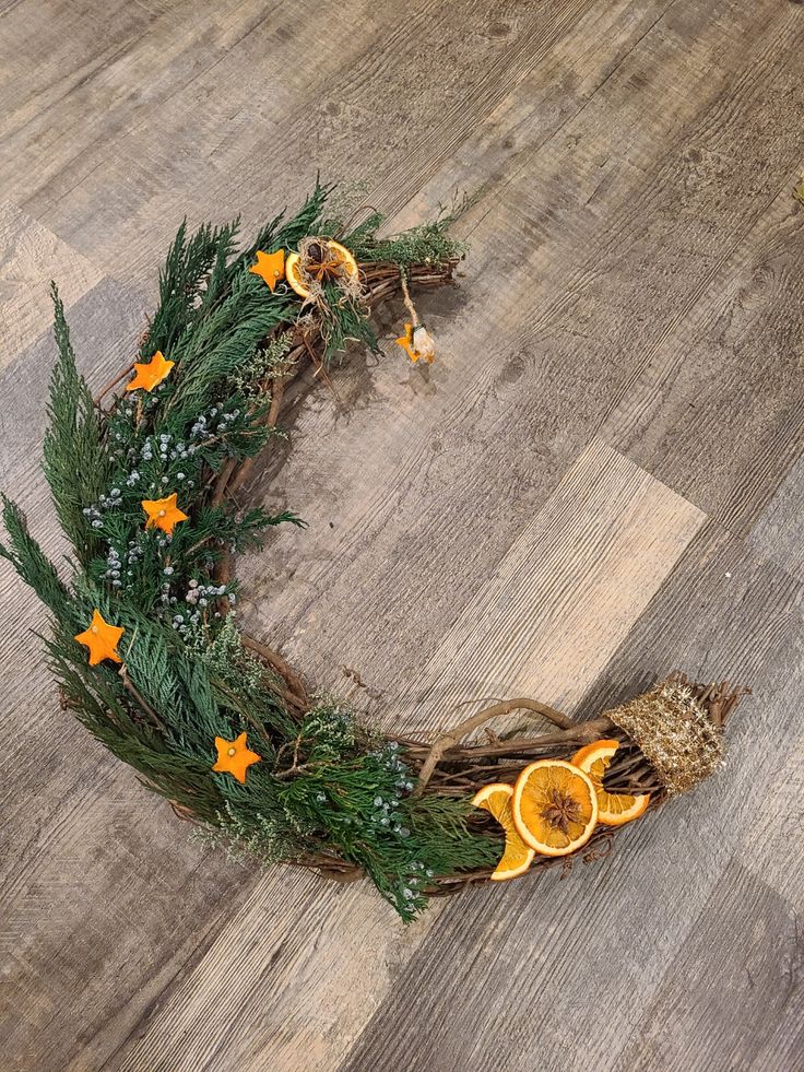 an orange and fir wreath on a wooden floor with star decorations around the edges,