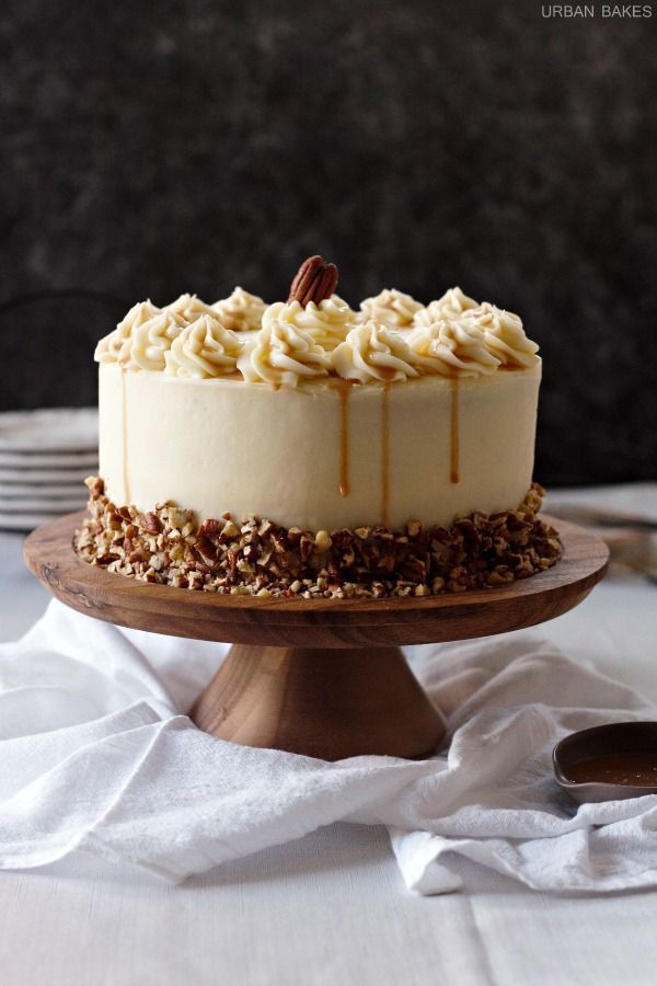 a cake sitting on top of a wooden plate covered in frosting and pecans