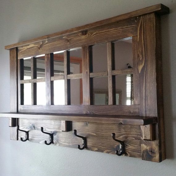 a wooden wall mounted shelf with hooks and mirrors on it's sides, hanging from the wall