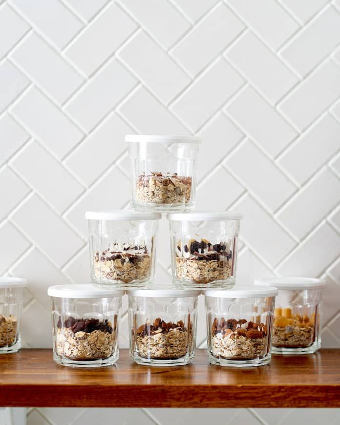 several glass containers filled with granola sitting on top of a wooden table next to a white tiled wall