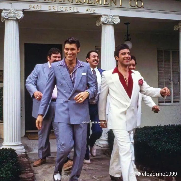 two men in suits are walking down the street with one man wearing a white suit and red shirt