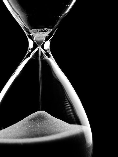 black and white photograph of an hourglass with sand running through the bottom, in front of a dark background