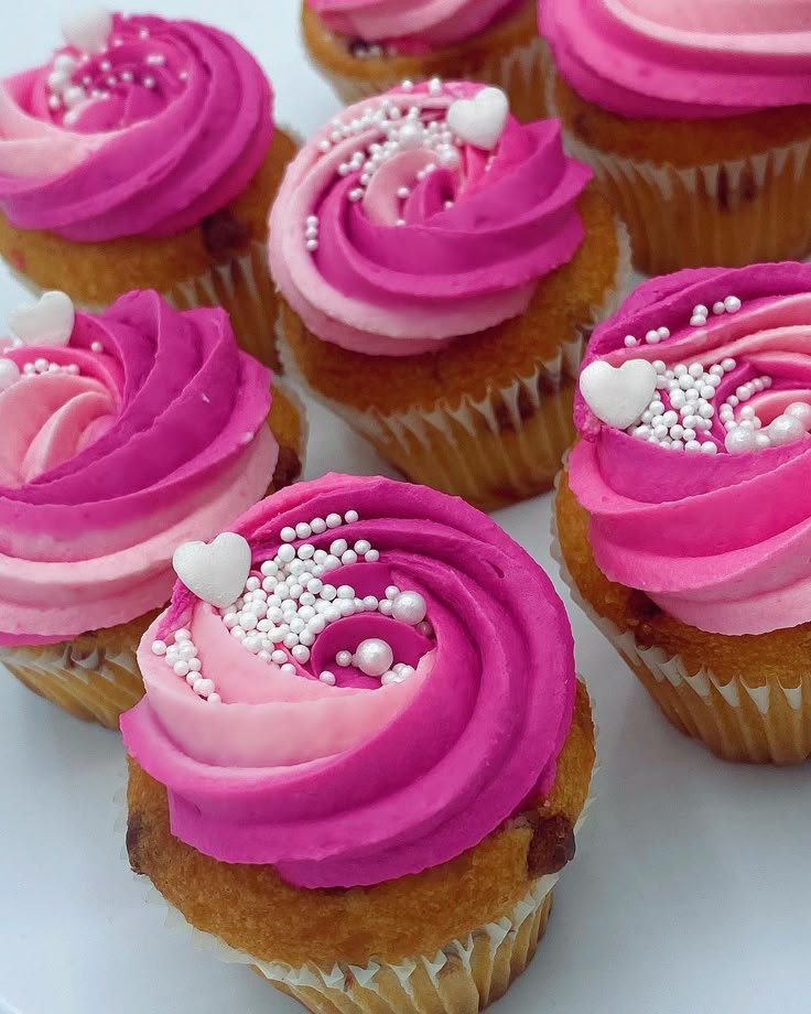 several cupcakes with pink frosting and white sprinkles on them