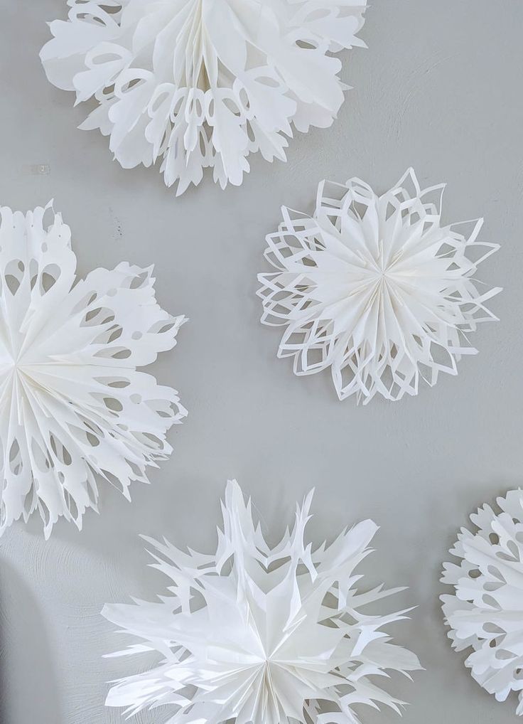 four white paper snowflakes hanging on the wall in front of a gray background