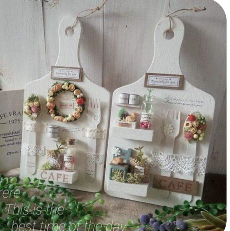 two white ceramic plaques with flowers and wreaths hanging from the sides on a table