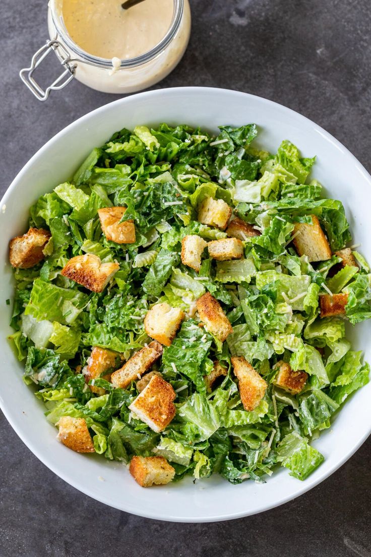 a white bowl filled with lettuce and croutons next to a cup of coffee