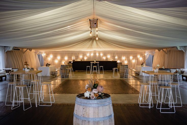 the inside of a tent with tables and stools in front of white drapes