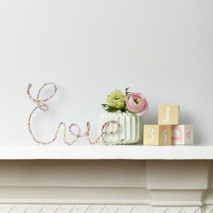 a white shelf topped with pink and green flowers next to a wooden block spelling the word ella