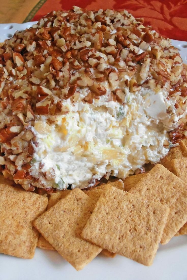 a white plate topped with crackers and cheese covered in nuts next to crackers