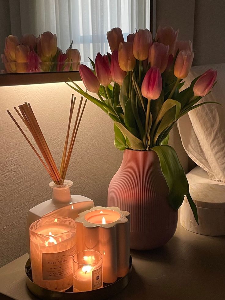 candles and flowers on a table in front of a mirror with a vase full of tulips