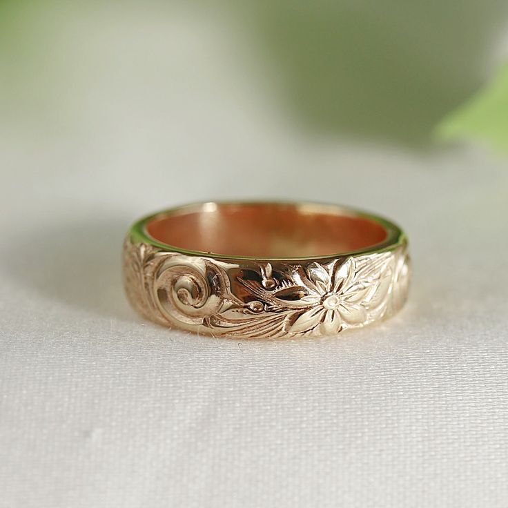 a gold wedding ring sitting on top of a white cloth covered table next to a green leafy plant