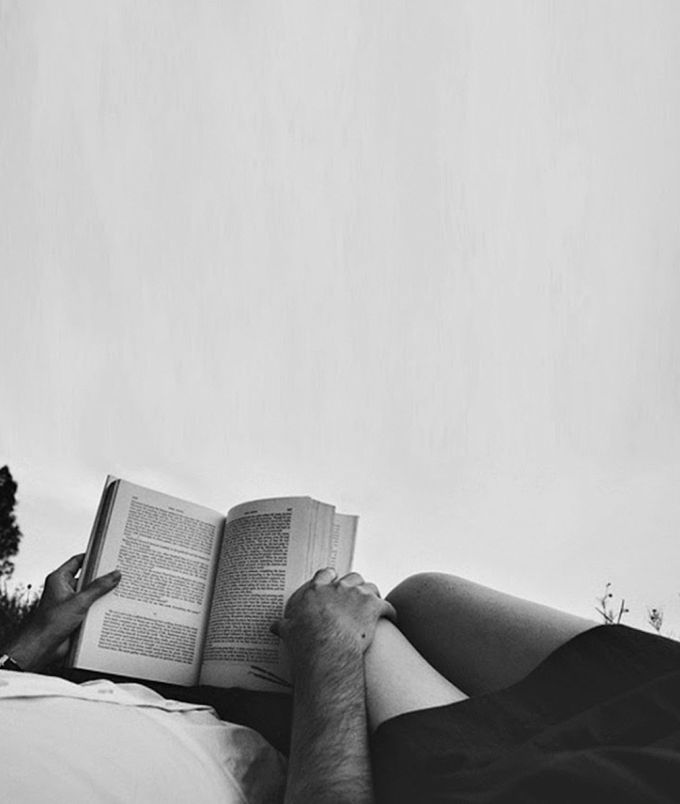 a man laying on top of a bed holding an open book in his hand and reading it