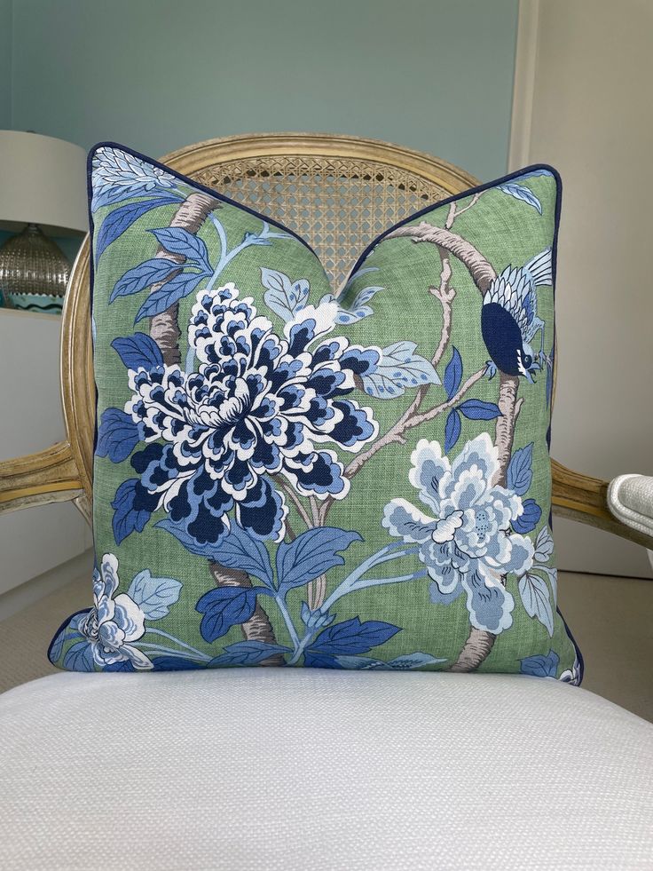 a blue and white flowered pillow sitting on top of a chair next to a lamp