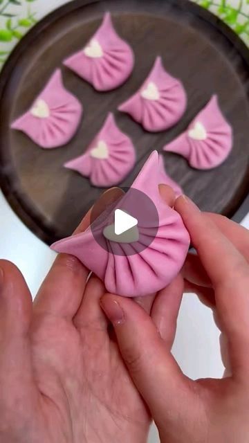 someone is decorating small pastries with pink icing on a cake pan and green leaves