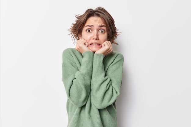 a woman in a green sweater holding her hands to her face and making a surprised expression