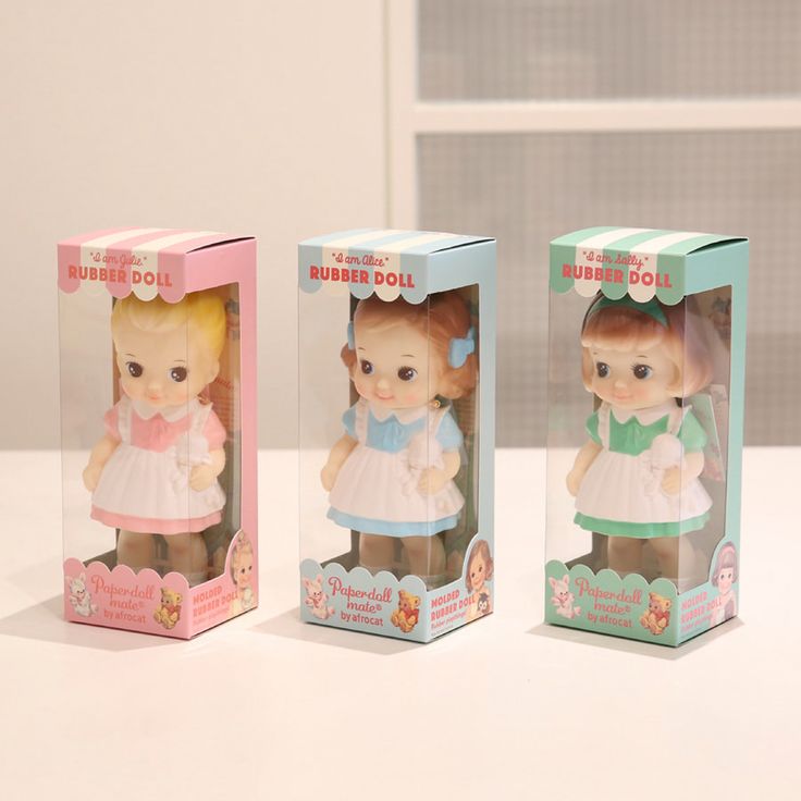 three little dolls in boxes sitting on a white table with one doll inside the box