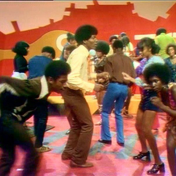 the group of people are dancing together on the floor in front of an orange and red wall