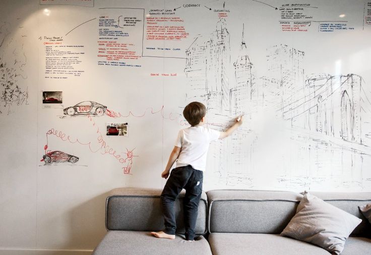 a young boy standing on top of a couch in front of a whiteboard wall