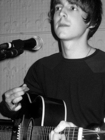 a young man playing an acoustic guitar in front of a microphone