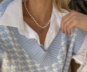 a woman wearing a blue and white sweater with a pearl necklace on her left shoulder