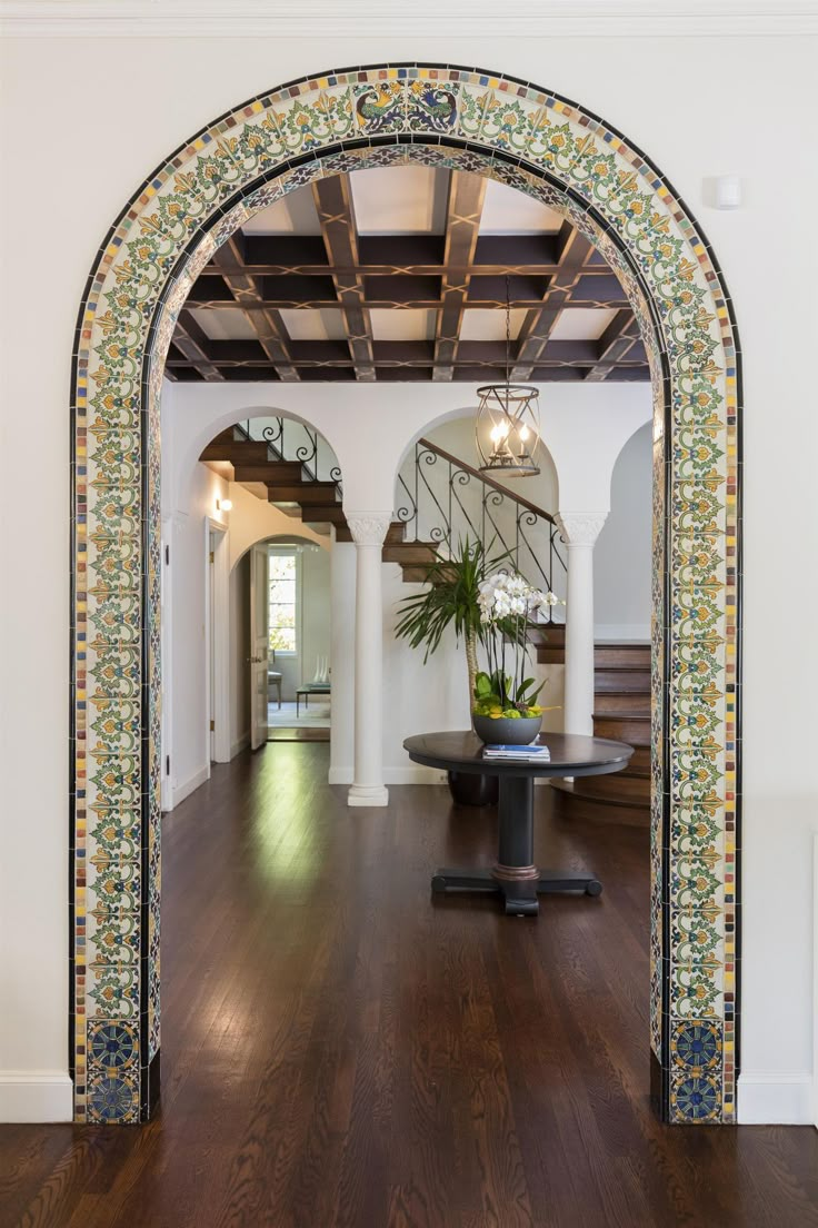 an archway in the middle of a room with wood floors and tile work on it