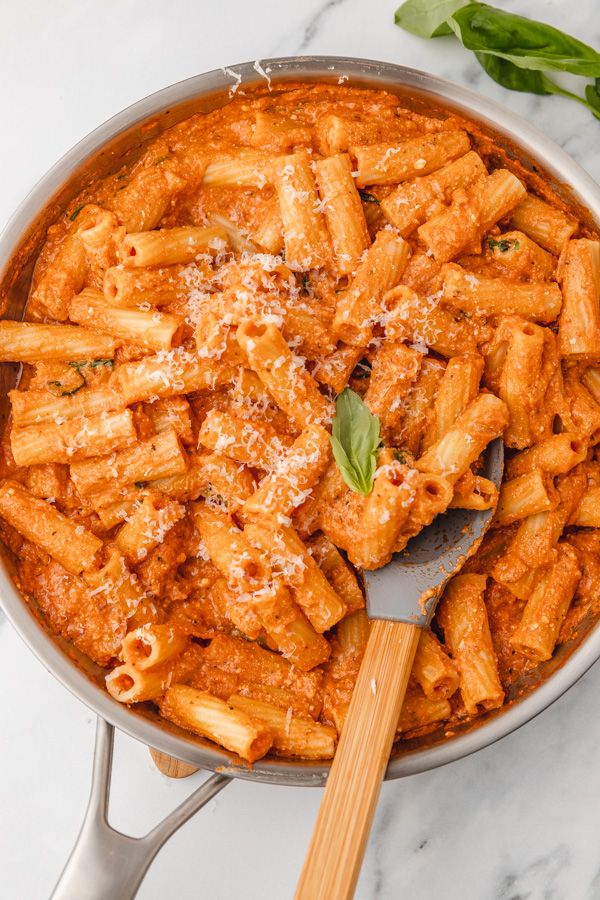 a pan filled with pasta and sauce on top of a table next to a wooden spoon