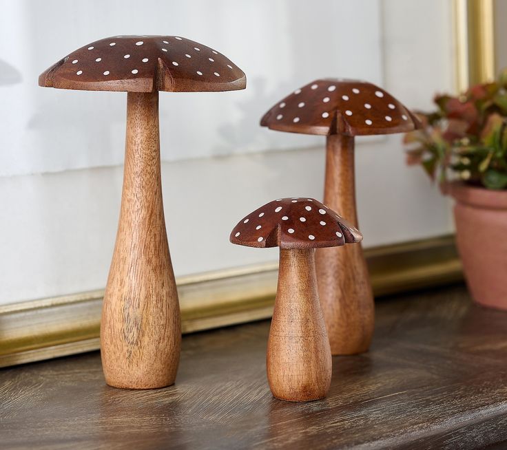 three wooden mushrooms sitting on top of a table next to a potted plant in front of a mirror