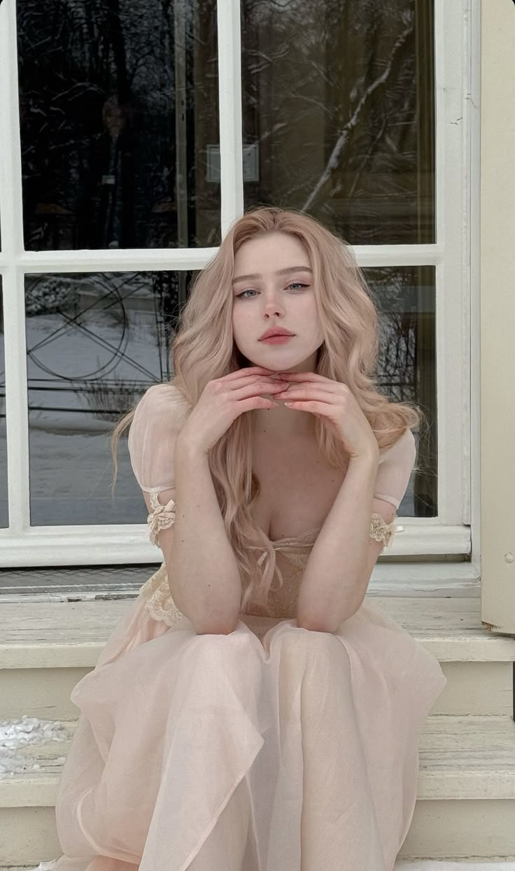 a woman sitting on the steps in front of a window with her hands under her face