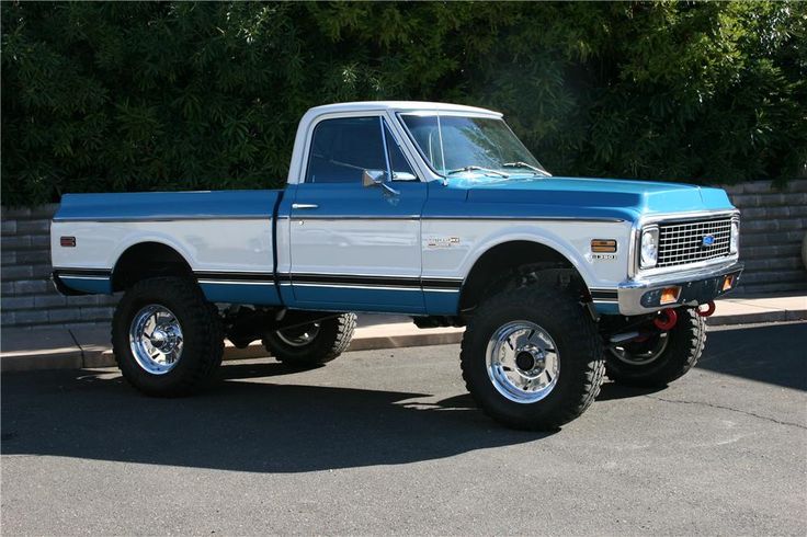 a blue and white pickup truck parked in a parking lot next to a brick wall