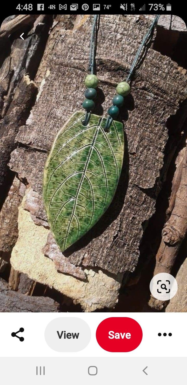 a green leaf is hanging from a necklace on a piece of wood with beaded beads