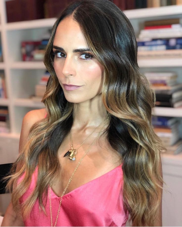 a woman with long brown hair standing in front of bookshelves wearing a pink dress