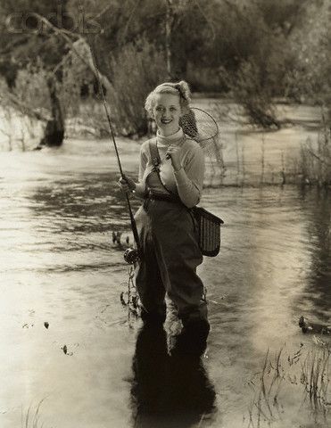 an old photo of a woman holding a fishing rod and smiling at the camera while standing in shallow water