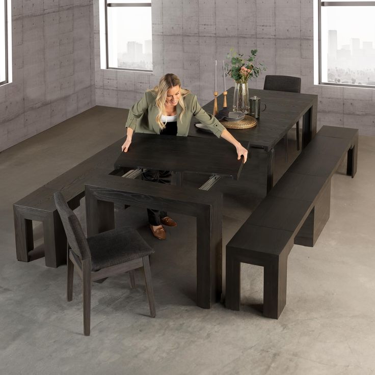 a woman sitting at a black table with two chairs and a vase on top of it