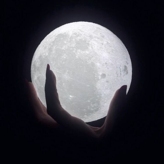 someone is holding the moon in their hands with both hands, and it appears to be dark